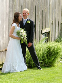 Bride and groom beside barn and ferns